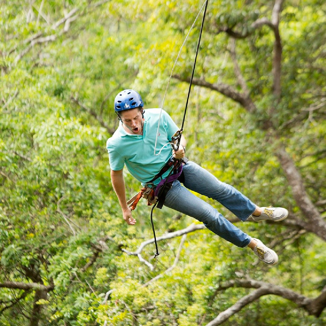 Guest in a helmet and harness swinging on a rope above the forest canopy on an adventure tour in Guanacaste, Costa Rica