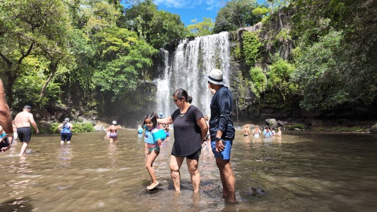 Family with a young girl in a life vest wading in the pool at Llanos de Cortés Waterfall, Guanacaste, Costa Rica