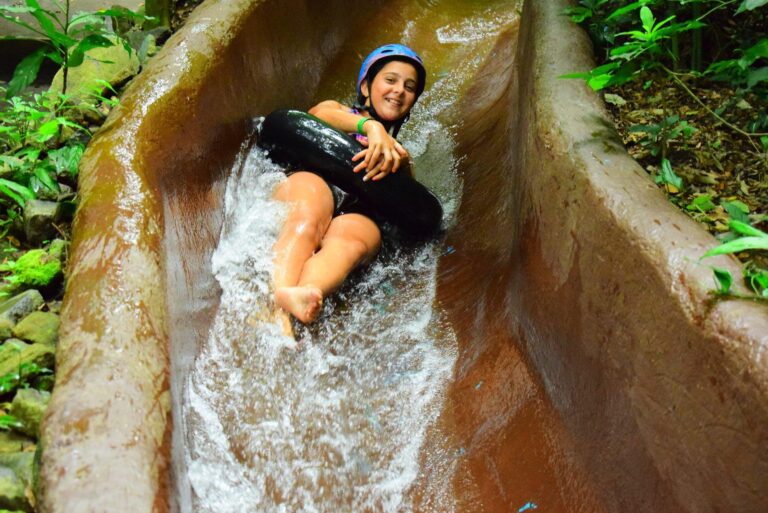 Smiling girl in a helmet riding an inner tube down a forest waterslide at Rincón de la Vieja, Costa Rica