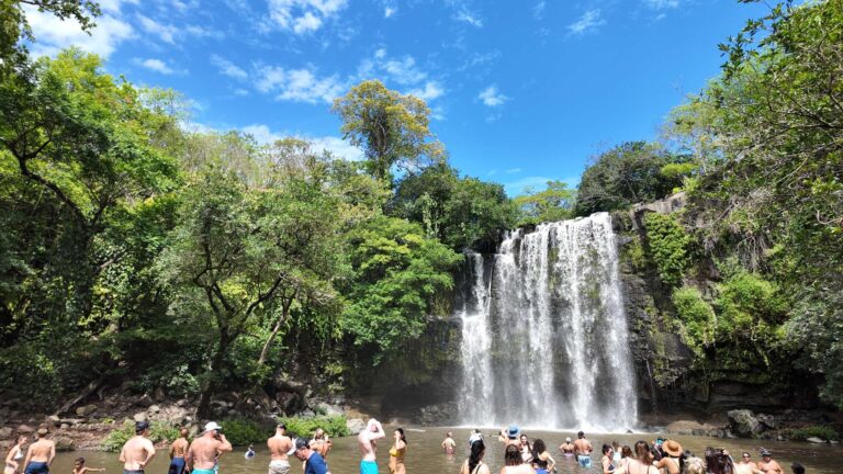 Visitors swimming in front of the wide curtain of Llanos de Cortés Waterfall, Guanacaste, Costa Rica
