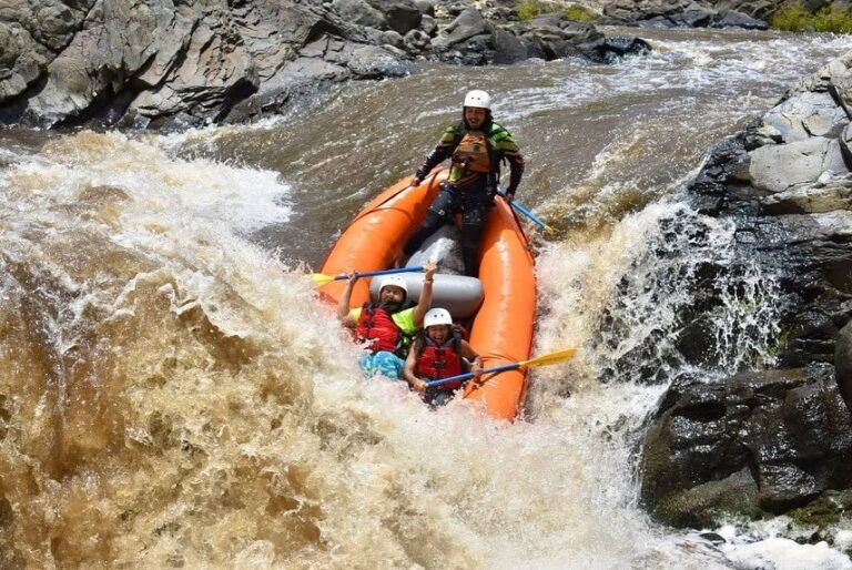 Guide and guests in an orange raft going over a drop in the brown high water of the Tenorio River, Costa Rica