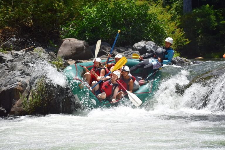 Group in a green raft with their guide going through a rapid between rocks on the Tenorio River, Costa Rica