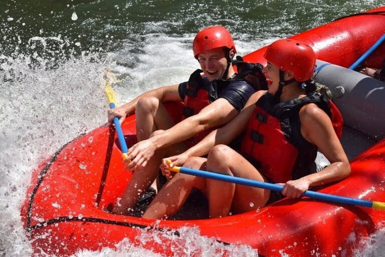 Two guests laughing as water splashes over their red raft on the Tenorio River, Costa Rica