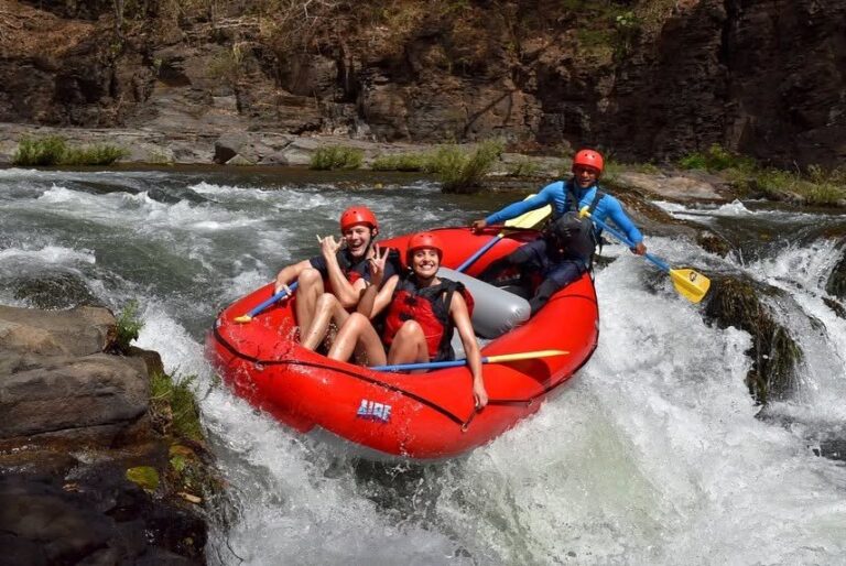 Two guests and their river guide smiling in a red raft on a rapid of the Tenorio River, Costa Rica