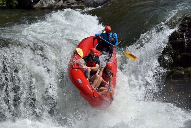 Red raft tipping over a waterfall drop with guests and guide on the Tenorio River, Costa Rica