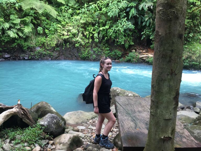Guest standing on the rocky bank of the sky-blue Río Celeste near Bijagua, Costa Rica