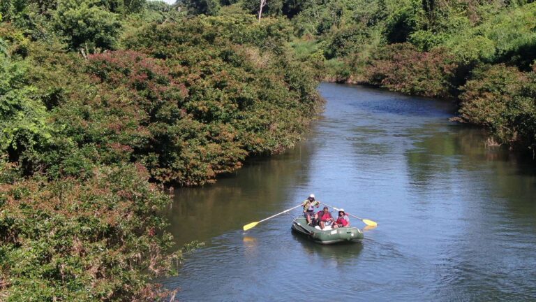 Guide rowing a raft with guests down a calm river lined with forest on a safari float in Guanacaste, Costa Rica