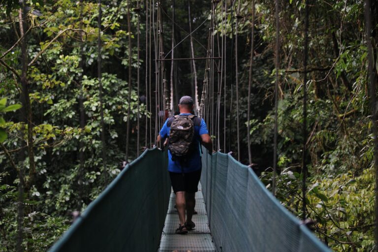 Guest with a backpack walking across a hanging bridge in the rainforest near Tenorio Volcano, Costa Rica
