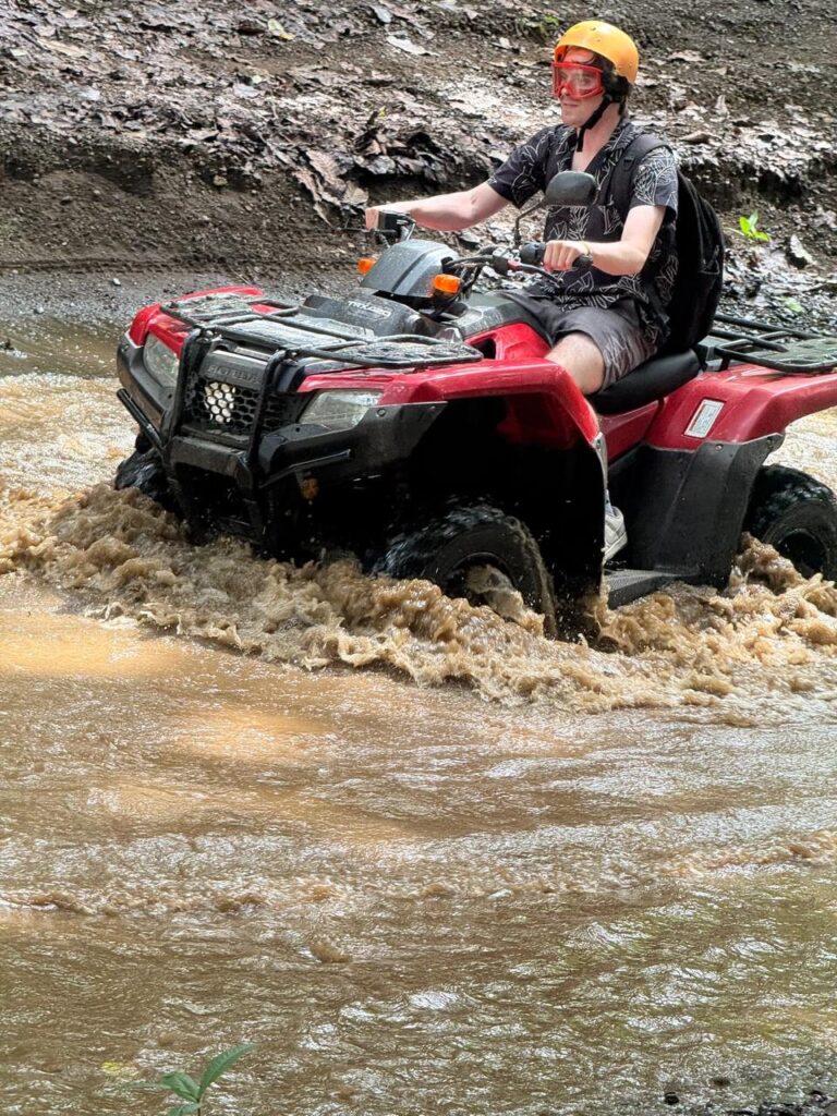 Rider with helmet and goggles driving an ATV across a river in Guanacaste