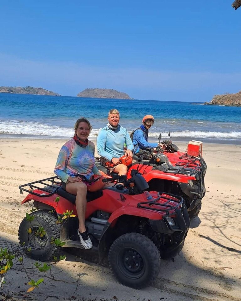 Guests on red ATVs on a white sand beach with islands in the background in Guanacaste