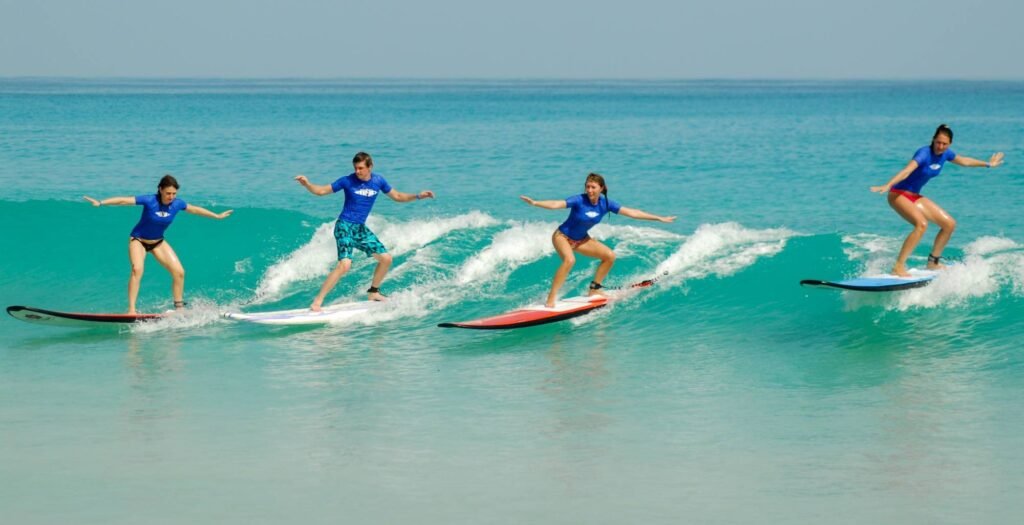 Four beginners standing on surfboards and riding a small wave during a surf lesson