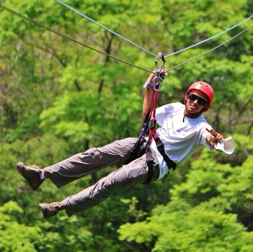 Smiling man in a red helmet riding a zip line over the forest canopy in Guanacaste