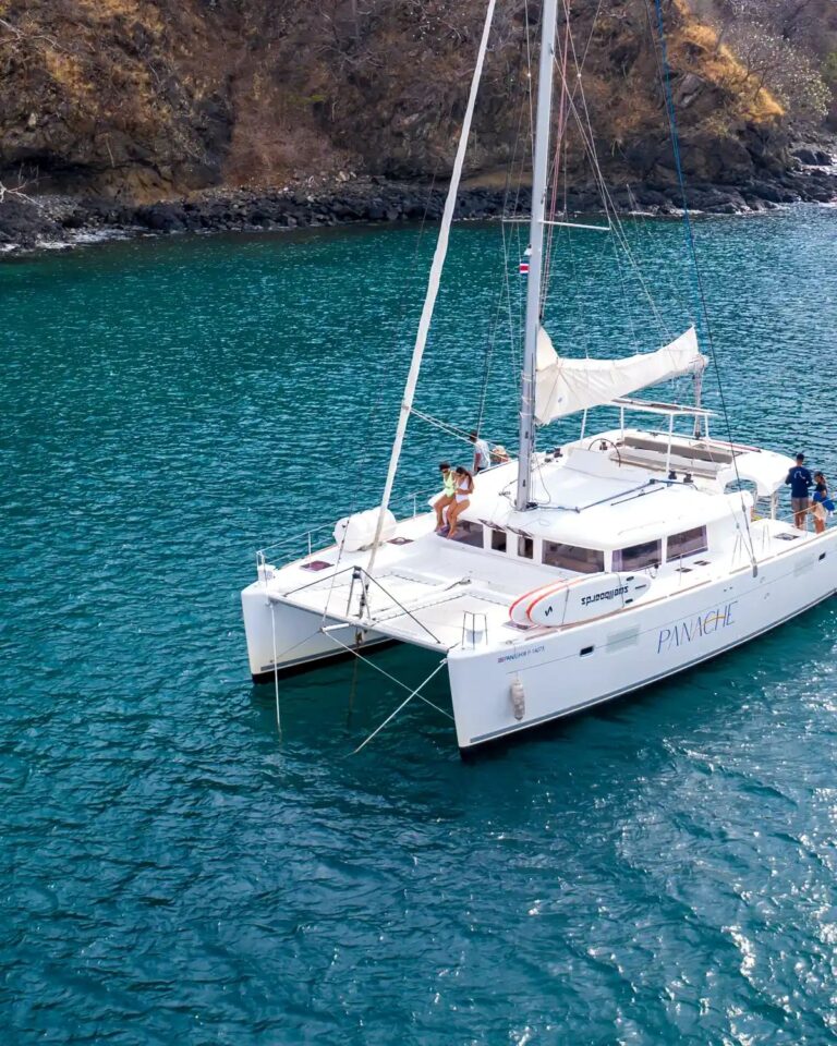 Catamaran anchored in turquoise water below a rocky dry-forest cove in Guanacaste, Costa Rica