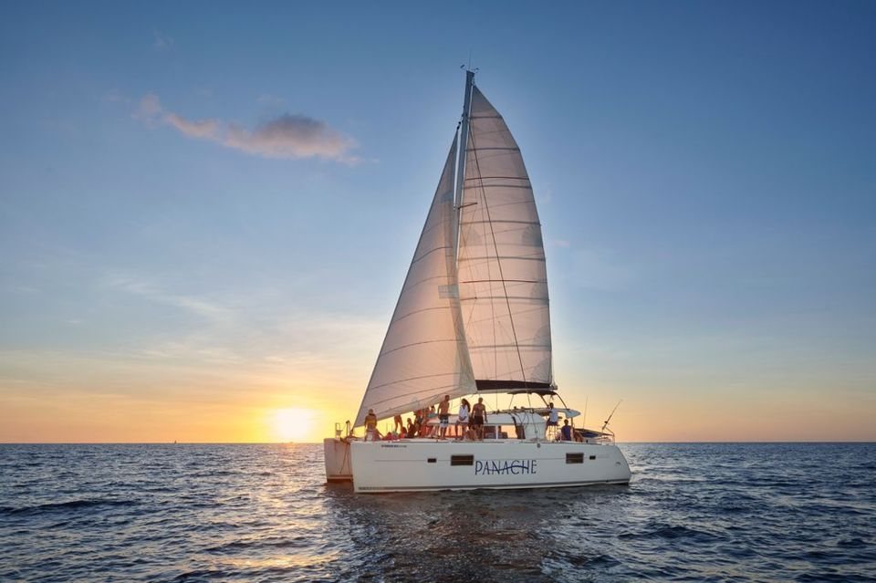 Catamaran with full sails and guests on deck as the sun sets over the Pacific Ocean, Costa Rica