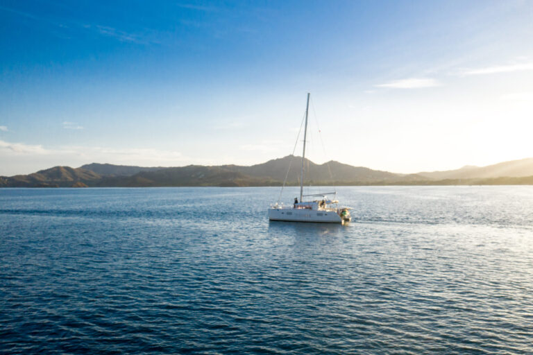 Catamaran sailing on calm blue water with the Guanacaste hills behind at golden hour, Costa Rica