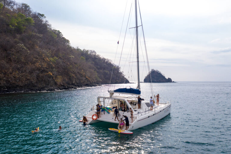 Catamaran anchored for a snorkel stop below the dry-forest coastline of Guanacaste, Costa Rica