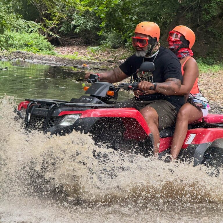 Couple riding a double ATV through a river with a big splash in Guanacaste