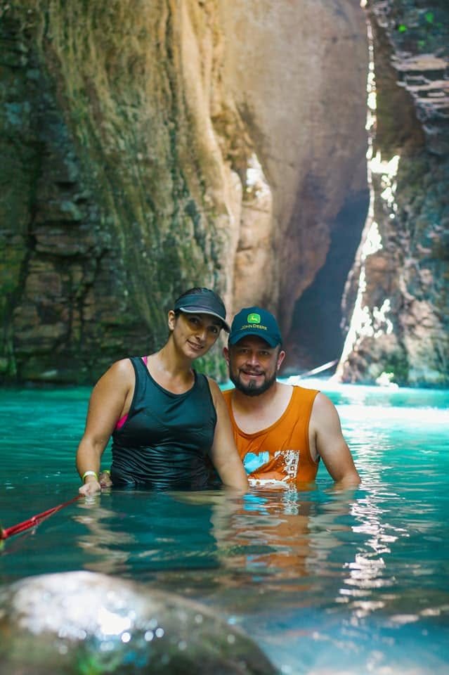 Couple in the turquoise water of the slot canyon at La Leona, holding the rope