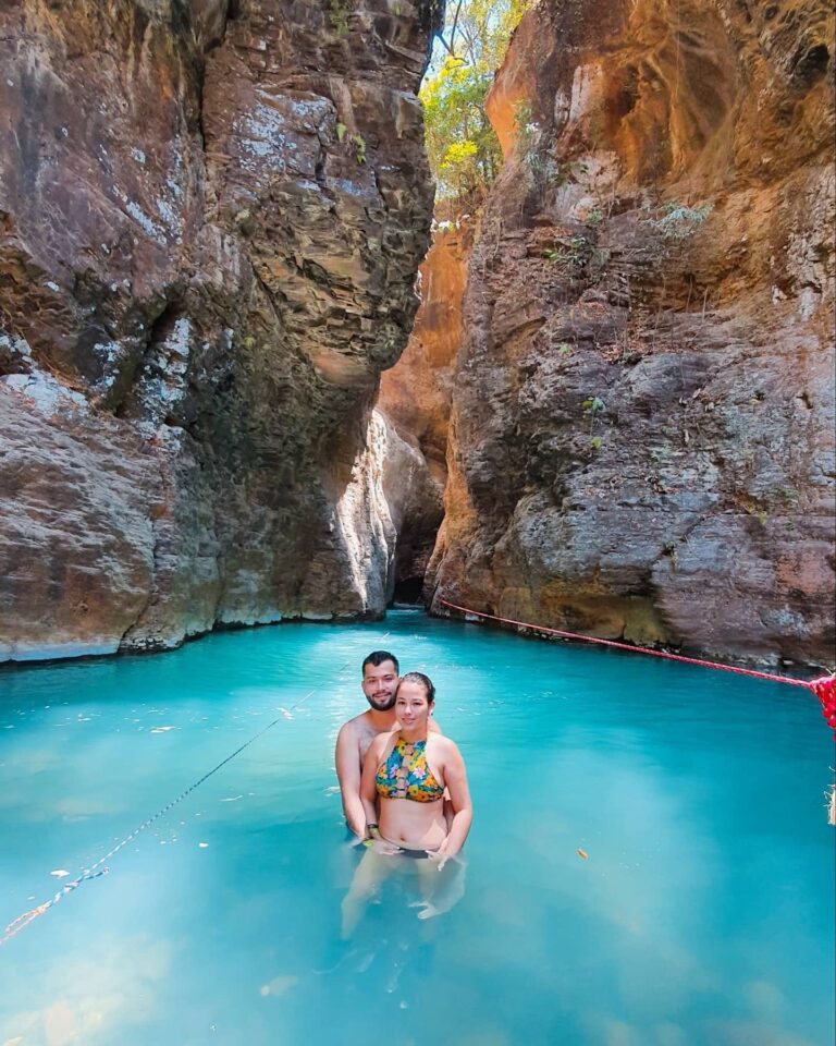 Couple standing in turquoise water at the entrance of the canyon to La Leona Waterfall