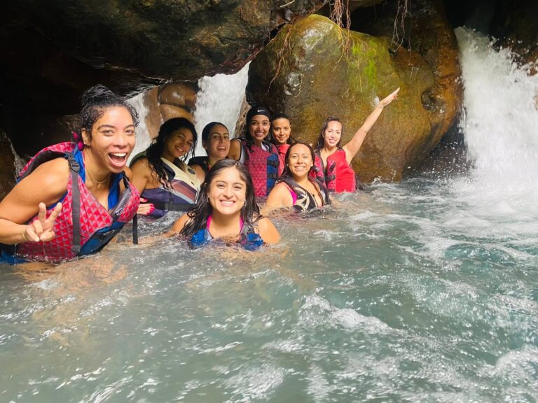 Group of friends in life jackets smiling beside a hidden waterfall on the Río Blanco