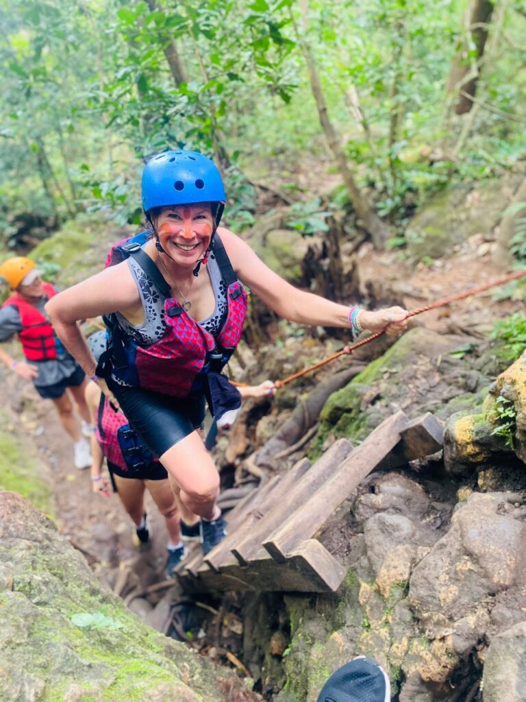 Guest in a helmet and life jacket climbing a wooden ladder with a rope on the La Leona trail