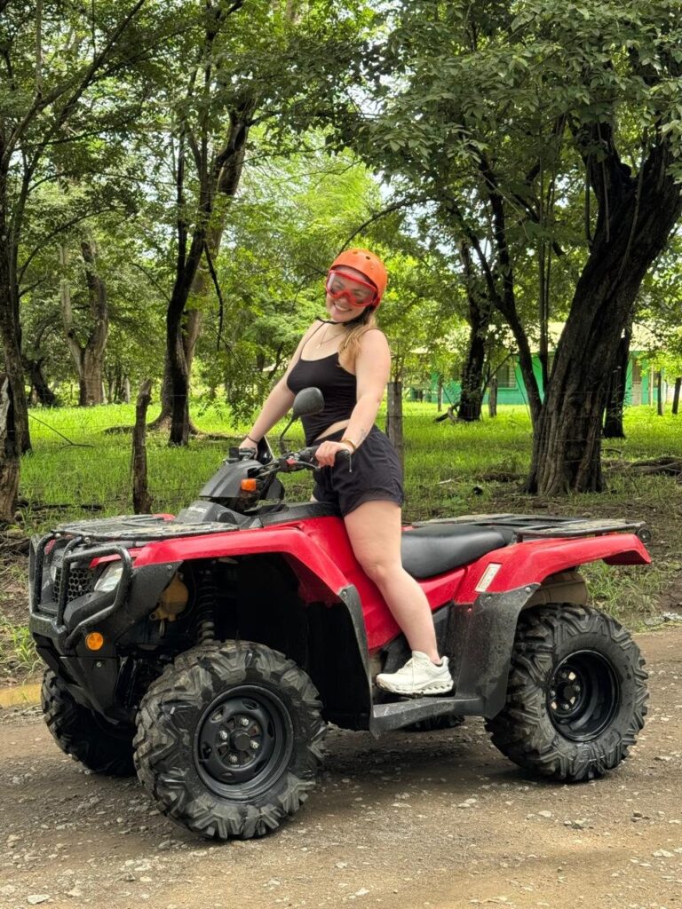 Smiling guest with helmet and goggles sitting on a red ATV on a country trail in Guanacaste