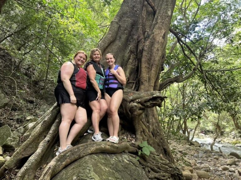 Three guests standing on the roots of a giant tree beside the Río Blanco trail