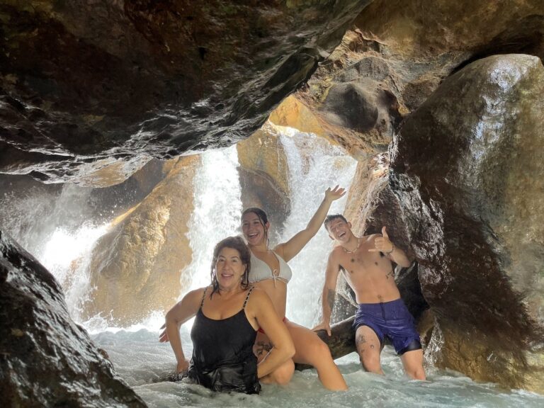 Three guests in a rock cave with a hidden waterfall behind them on the Río Blanco