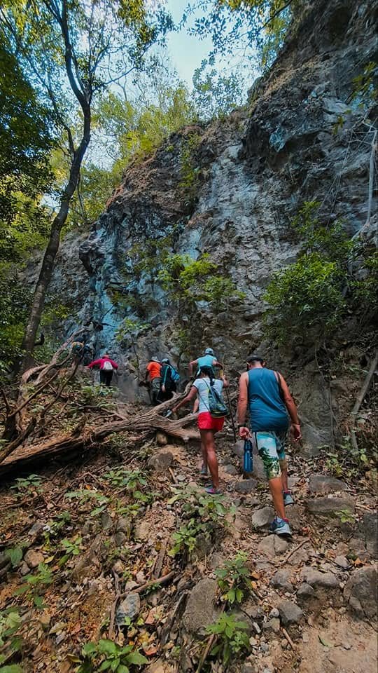 Hikers climbing a rocky forest trail below a cliff on the way to La Leona Waterfall