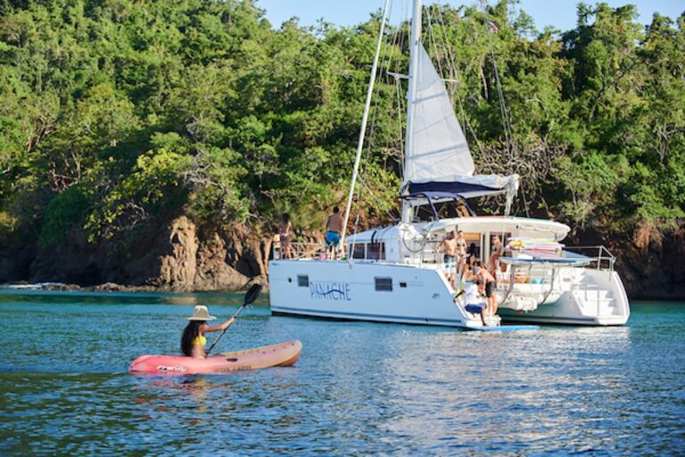 Guest in a kayak paddling toward the catamaran anchored in a forested cove in Guanacaste, Costa Rica