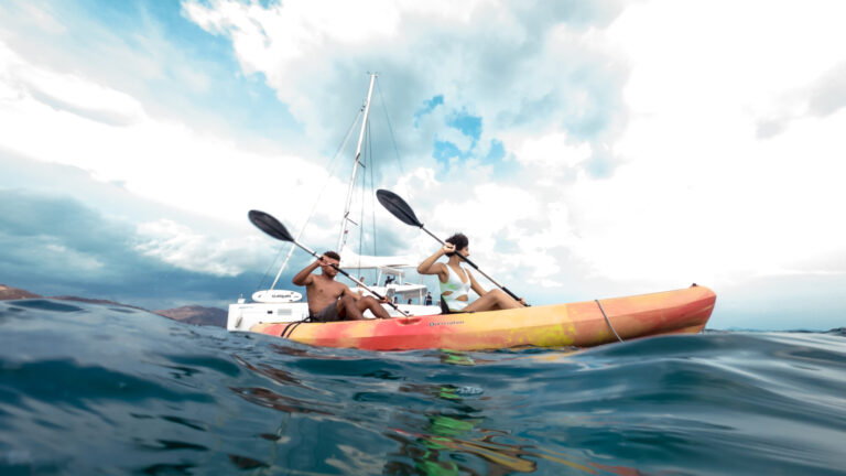 Two guests paddling a tandem kayak beside an anchored catamaran on the Pacific in Guanacaste, Costa Rica