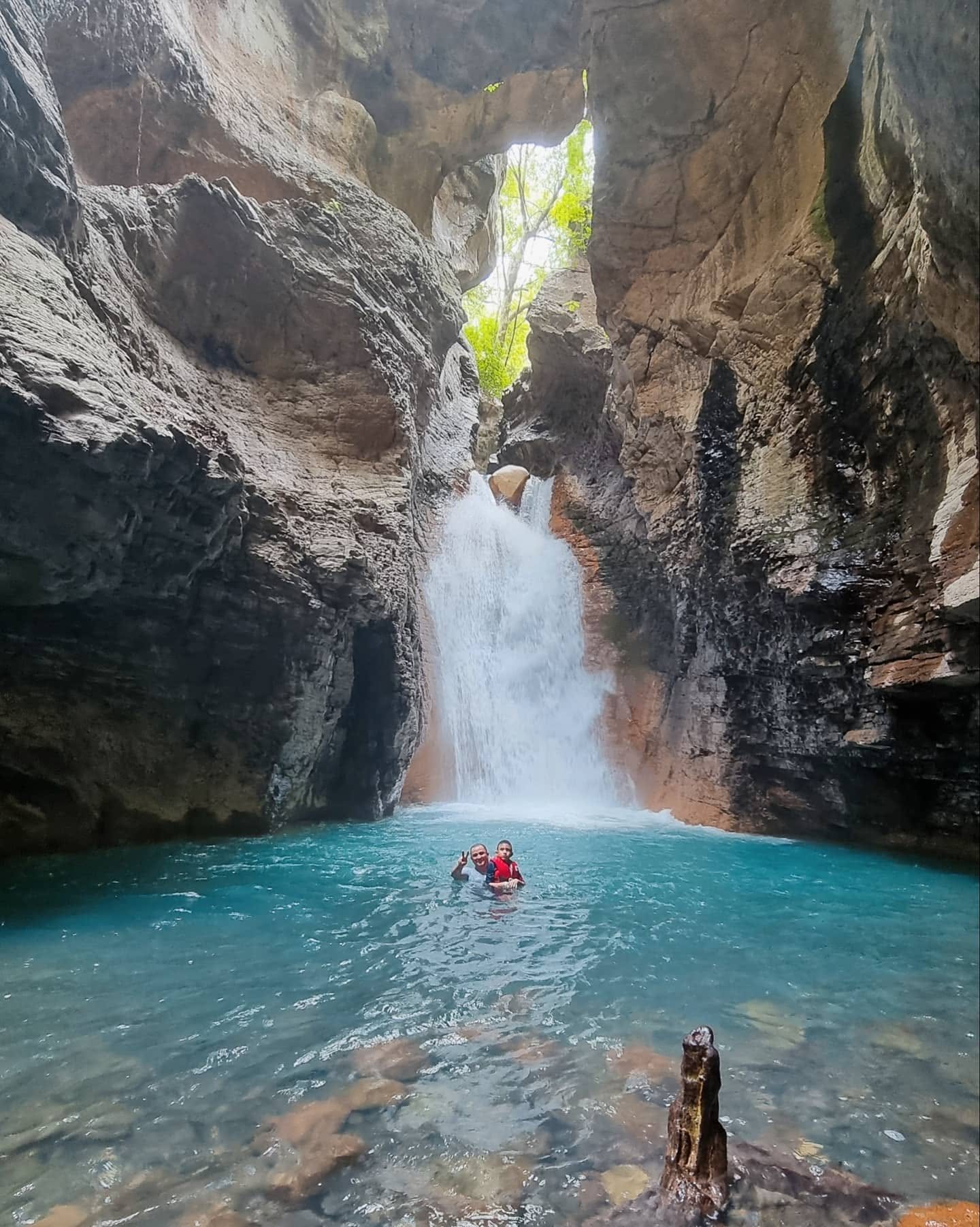 La Leona Waterfall falling into a turquoise pool inside the canyon, with two swimmers