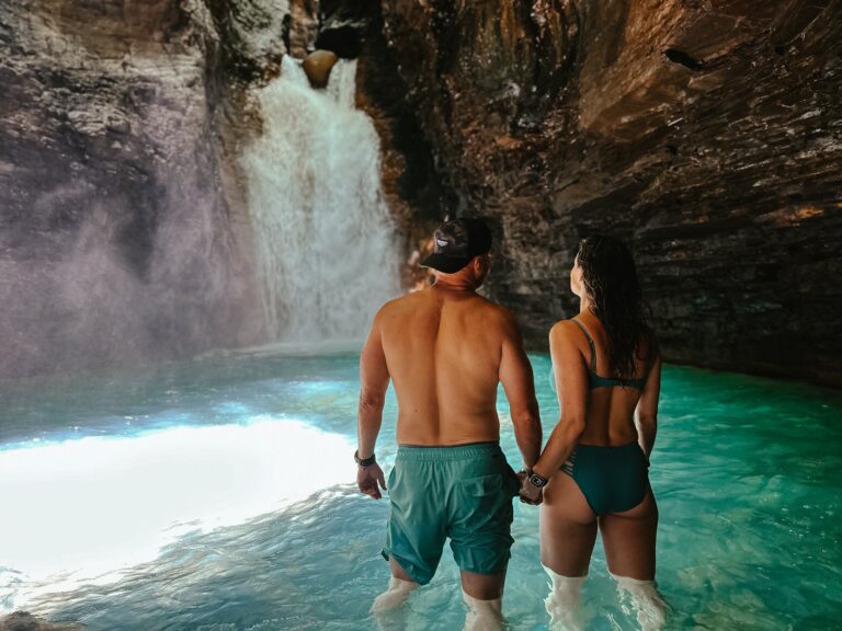 Couple standing in the turquoise pool in front of La Leona Waterfall, Costa Rica