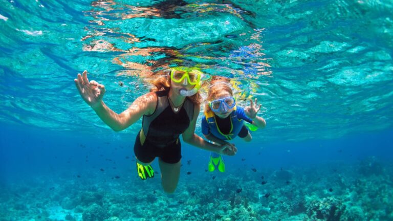 Mother and child snorkeling together over a coral reef, both making the OK sign