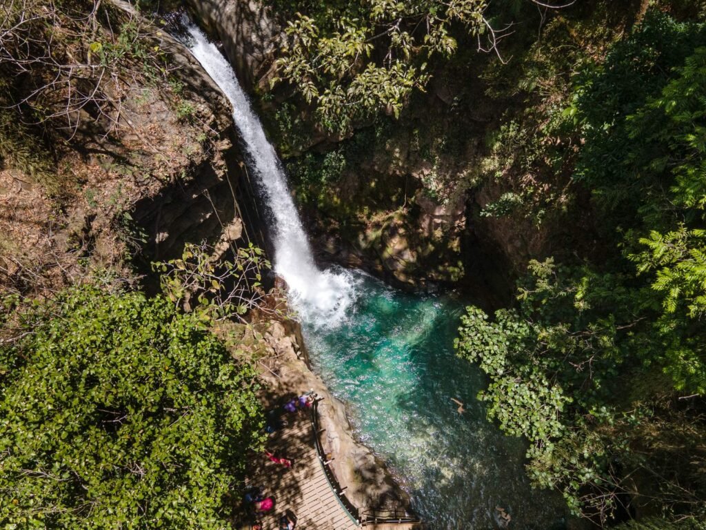 Aerial view of Oropéndola Waterfall dropping into its turquoise pool beside the wooden platform, Rincón de la Vieja, Costa Rica