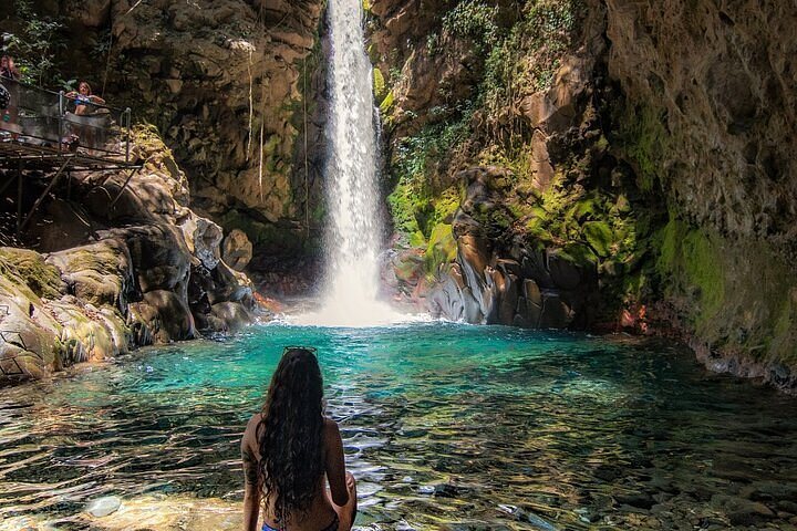 Guest sitting in the turquoise pool in front of Oropéndola Waterfall, Rincón de la Vieja, Costa Rica