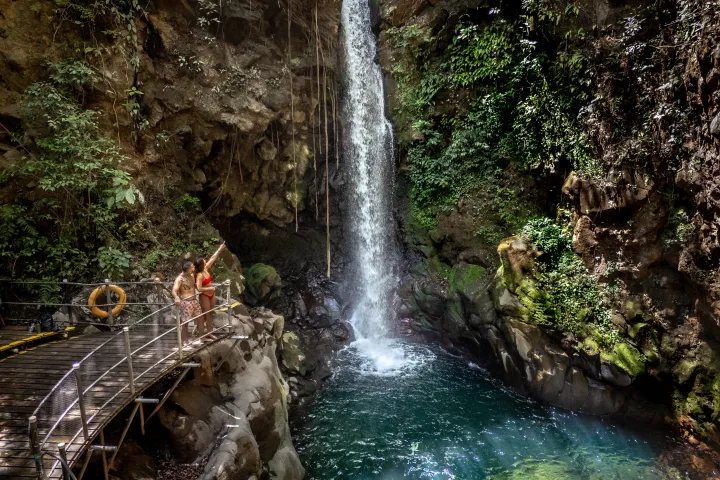 Two guests on the wooden platform beside Oropéndola Waterfall in its rocky canyon, Rincón de la Vieja, Costa Rica