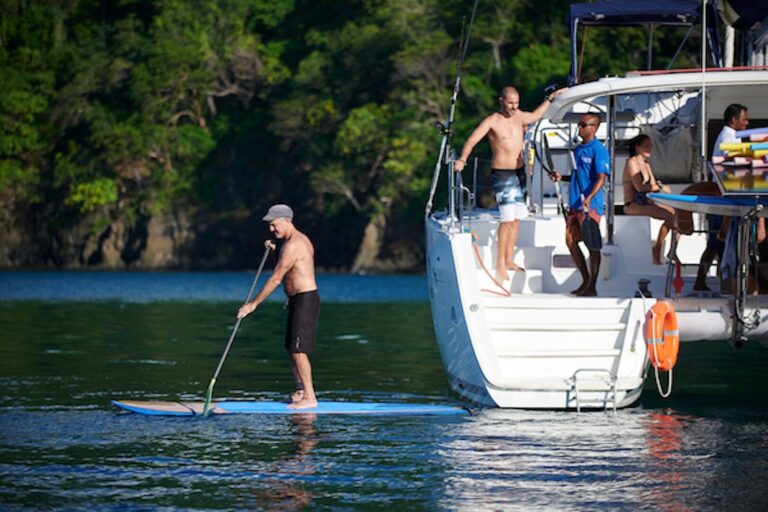 Guest stand-up paddleboarding next to the catamaran in a green, sheltered cove in Guanacaste, Costa Rica