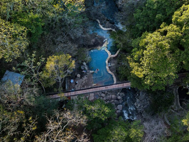 Top-down aerial view of the Río Negro hot spring pools and the hanging bridge in the dry forest, Rincón de la Vieja, Costa Rica