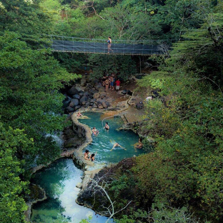 Aerial view of guests in the Río Negro hot spring pools under a hanging bridge in the forest, Rincón de la Vieja, Costa Rica