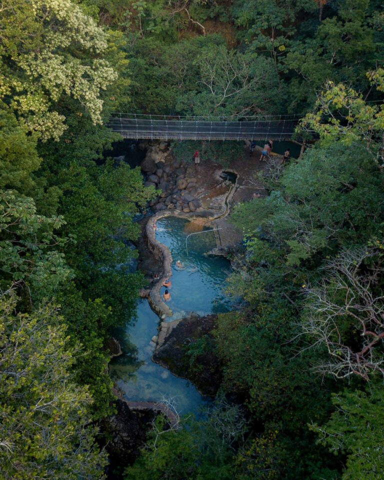 Aerial view of the blue Río Negro hot spring pools winding through the forest below a hanging bridge, Costa Rica