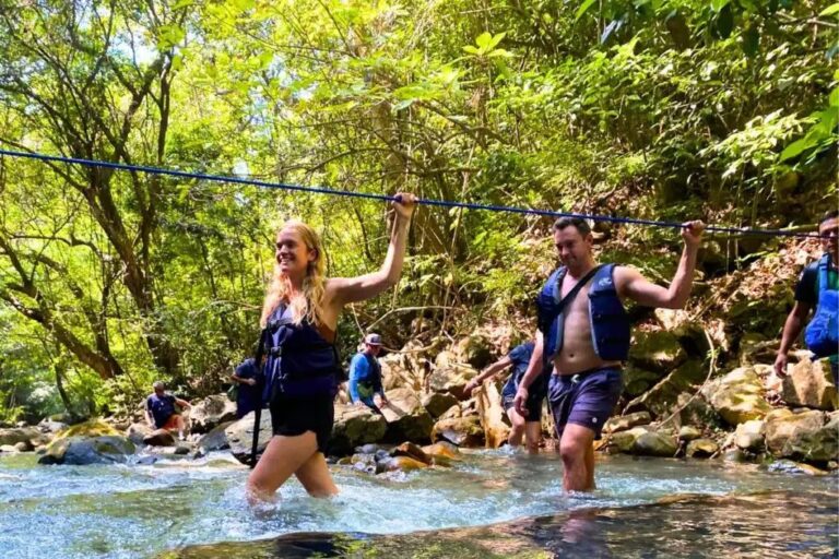 Hikers in life jackets crossing the Río Blanco holding a rope on the La Leona hike