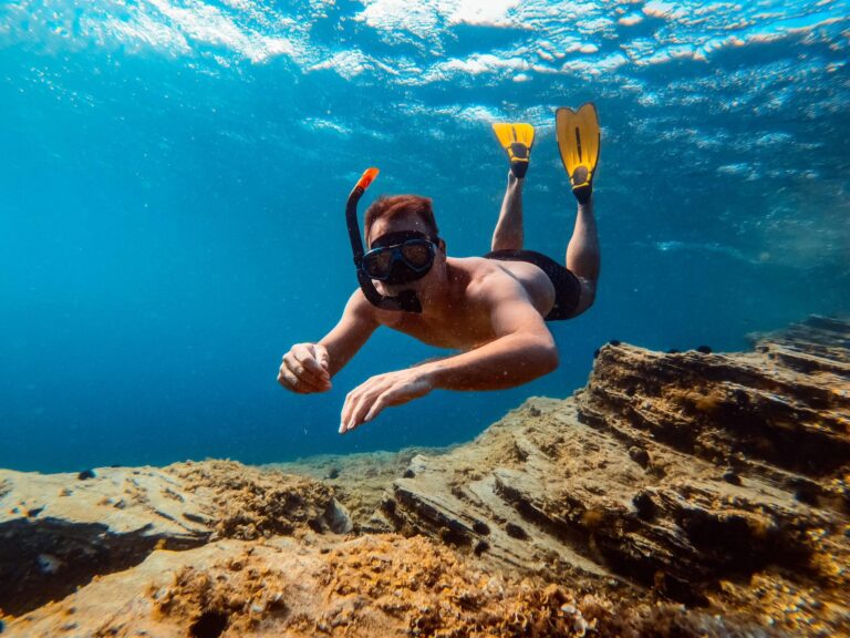 Snorkeler with yellow fins swimming along a rocky reef in blue water
