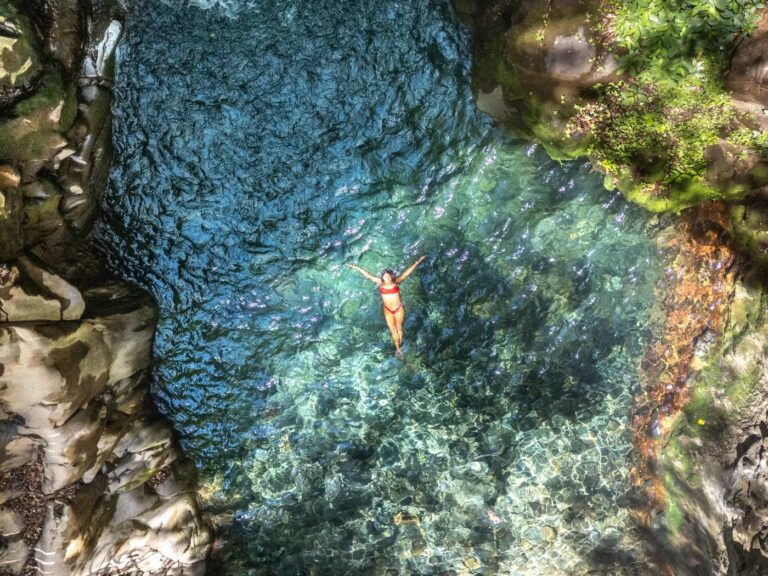 Aerial view of a guest floating in the clear turquoise pool of Oropéndola Waterfall, Rincón de la Vieja, Costa Rica
