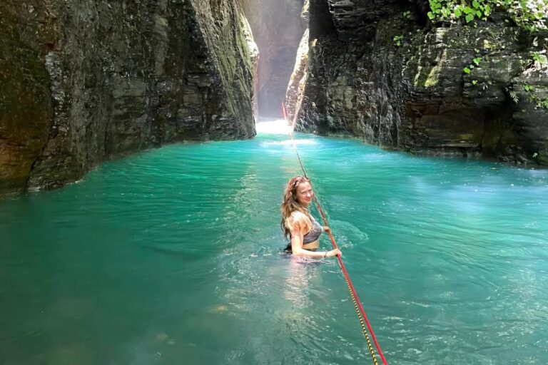 Woman holding the rope while swimming into the turquoise slot canyon at La Leona Waterfall