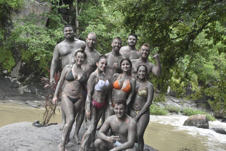 Group of guests covered in volcanic mud smiling on a rock beside the Río Negro, Rincón de la Vieja, Costa Rica