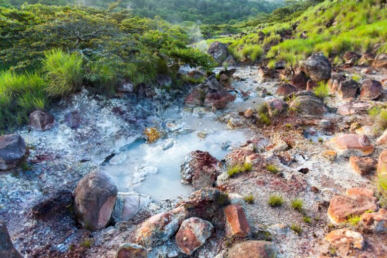 Milky volcanic mud pool among red and orange mineral-stained rocks in Rincón de la Vieja National Park, Costa Rica