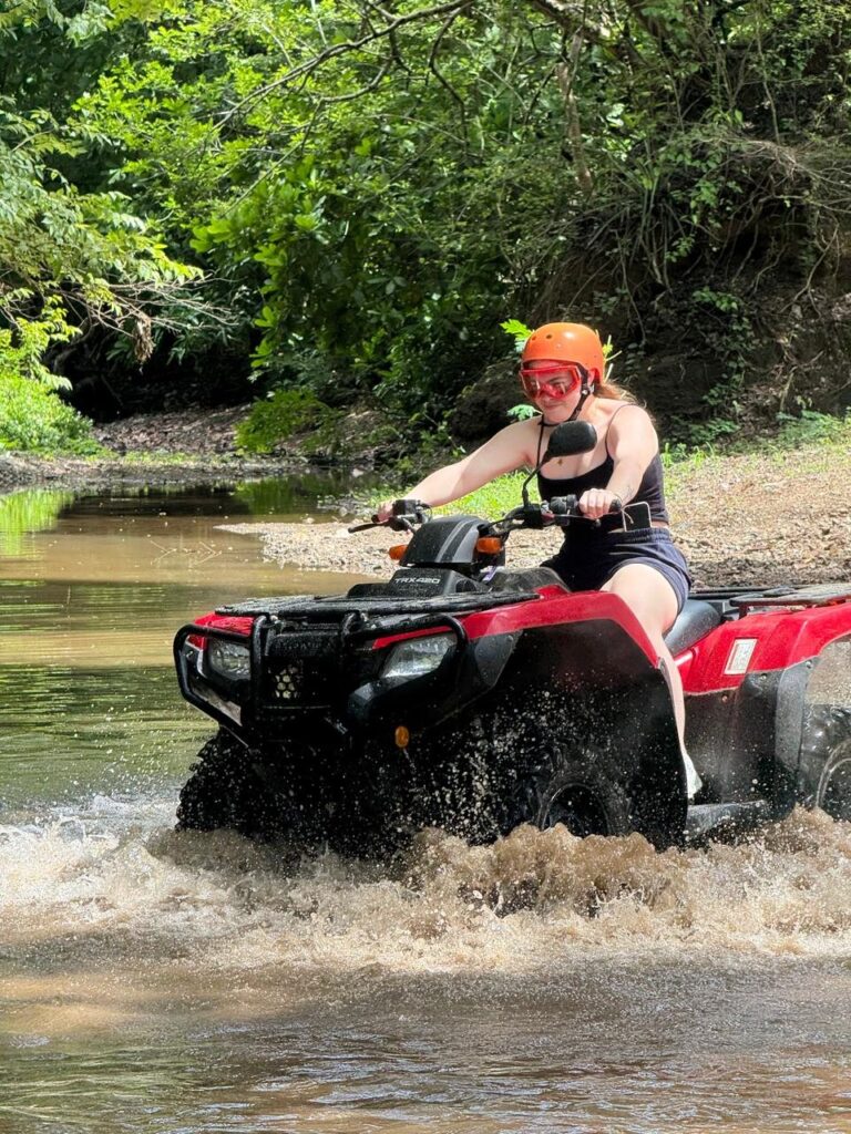 Woman riding a red ATV through a shallow river in the forest in Guanacaste